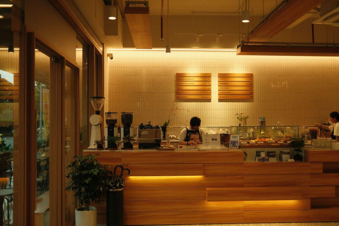 Two baristas at work behind a warm wooden counter.