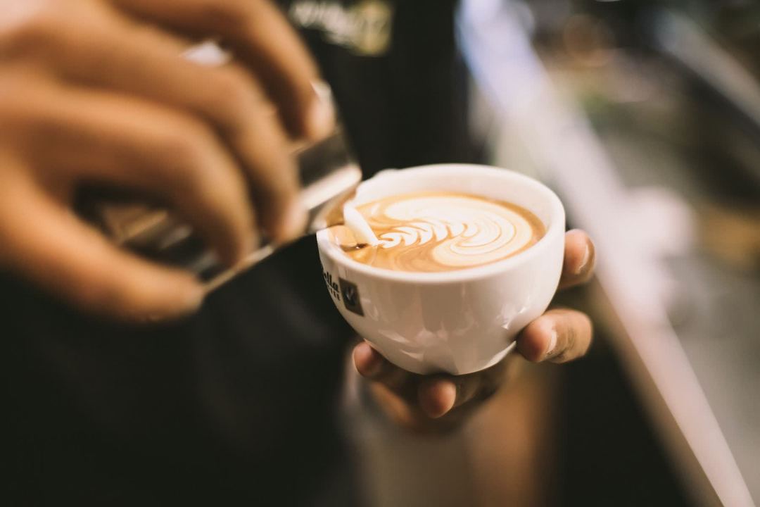 A barista pours steamed milk into a cup, the latte art settling in the crema.